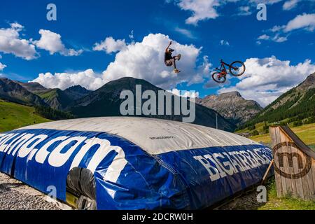 Ein Downhill-Radfahrer übt einen schwierigen Sprung mit der Sicherheit der Landung auf einem großen Airbag im Mottolino Bike Park, die Berge von Livi umgeben Stockfoto