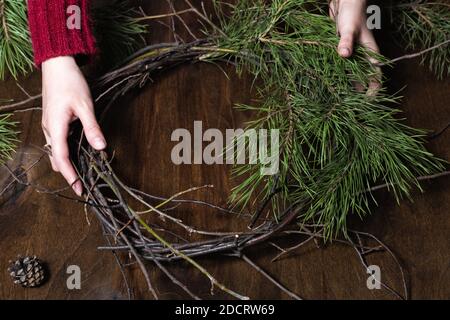 Frau macht weihnachtskranz aus Naturzweigen. Dunkler Holztisch Stockfoto