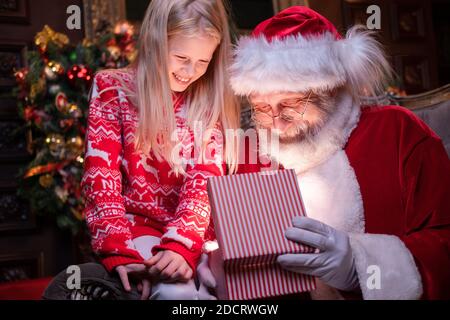 Weihnachtsmann und Mädchen Eröffnung Weihnachtsgeschenk in der Nähe Weihnachtsbaum. Magische Erfüllung der Wünsche Wünsche Stockfoto