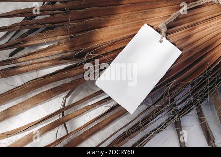 Unbeschriftete Geschenkidee, Modell mit Naturseil auf trockenen Palmblättern. Nahaufnahme leerer Papieretiketten bei Sonnenlicht mit Schatten. Tropisches Stillleben Stockfoto