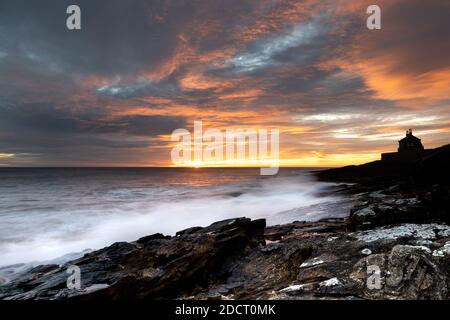 Sonnenaufgang in Northumberland bei Howick. Die Wellen stürzen in die felsige Küstenlinie, während die Sonne über der Nordsee aufgeht. Stockfoto