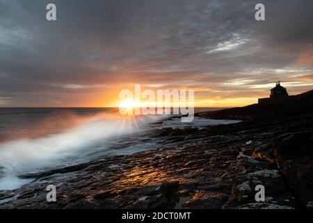 Sonnenaufgang in Northumberland bei Howick. Die Wellen stürzen in die felsige Küstenlinie, während die Sonne über der Nordsee aufgeht. Stockfoto