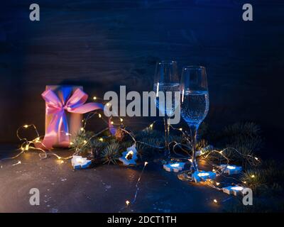 Feiern Sie Weihnachten, zwei Gläser Sekt in der Nacht auf einem Tisch mit Girlanden und farbigen Lichtern beleuchtet Stockfoto