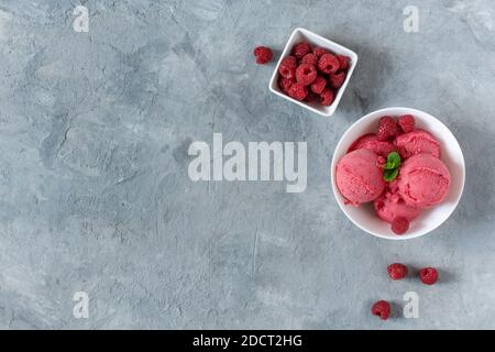 Schaufeln Himbeer-Eis in einem weißen Teller auf der grauen Tischansicht. Erfrischendes Sorbet im Sommer. Stockfoto