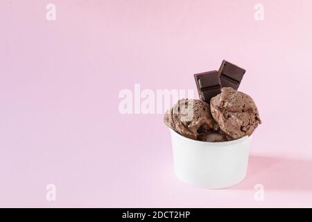 Kugeln Schokoladeneis in einem Papierbecher auf rosa Hintergrund. Eis zum Mitnehmen. Erfrischendes Sommerdessert. Stockfoto