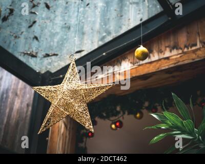 Weihnachtsschmuck. Großer Goldstern und Kugeln, Ornament hängt an der Gebäudestruktur im Gewächshaus Zimmer für Urlaub kommen. Stockfoto