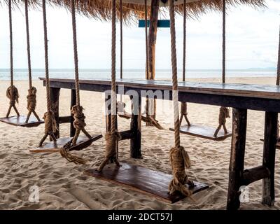 Leerer brauner Holztisch umgeben mit Holzschaukeln auf dem Strand Hintergrund. Stockfoto