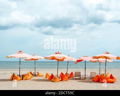 Orangefarbene Sonnenschirme und Sitzsäcke am Sandstrand auf blauem Himmel Hintergrund mit Kopierplatz, minimalistischer Stil. Stockfoto