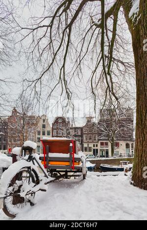 Geparktes Lastenfahrrad mit Schnee bedeckt vor einem Amsterdam Kanal im Winter Stockfoto