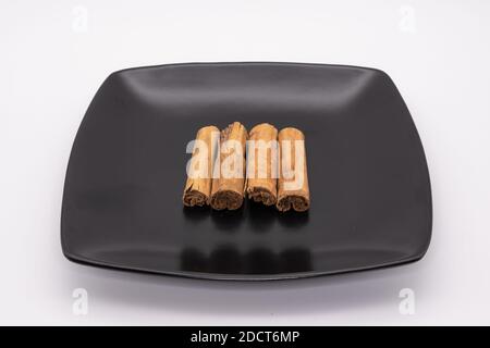Zimtstangen auf einem quadratischen schwarzen Teller gegen einen weißen Hintergrund Stockfoto