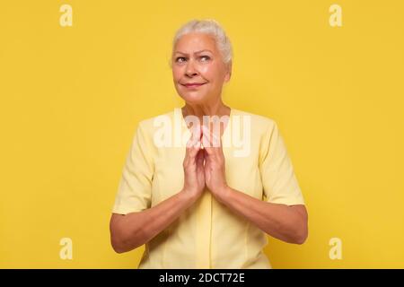 Ältere selbstbewusste und knifflige Frau hält die Finger zusammen und grinst beiseite, mit einigen kniffligen Idee Stockfoto
