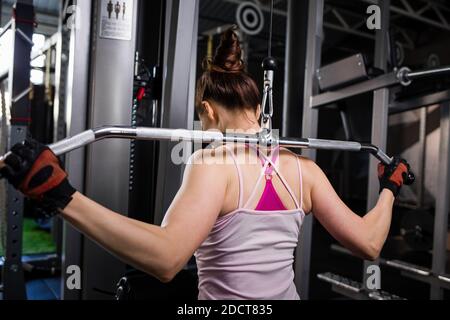 Junge Frau auf zieht nach unten Kabelmaschine im Fitnessstudio Stockfoto