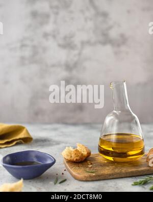 Olivenöl in der Flasche, frisches Baguette, Rosmarin. Grauer Hintergrund, vertikales Bild, Kopierraum Stockfoto