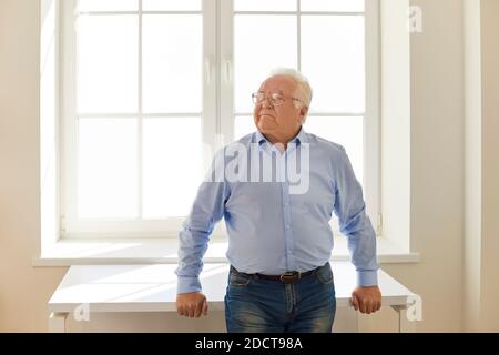 Selbstbewusster, seriöser älterer Mann, der in der Nähe des Fensters in neuem steht Haus und Blick weg Stockfoto