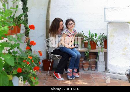 Glückliches Kind sitzt auf den Runden ihrer Mutter von Pflanzen und Blumentöpfen umgeben, Haus botanischen Konzept . Stockfoto