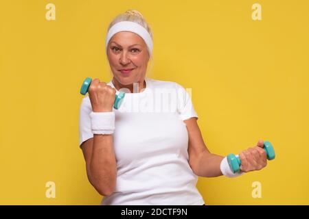 Reife Frau mit Hanteln auf gelbem Hintergrund Stockfoto