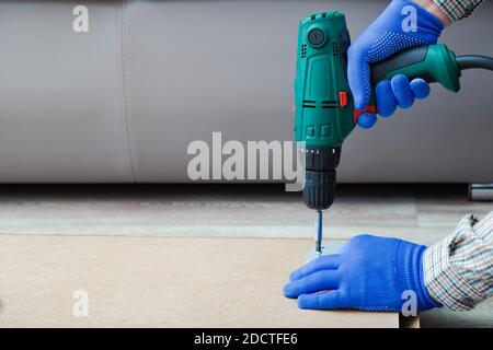 Der elektrische Bohrer arbeitet in Handmannhänden. Männliche Hände in Handschuhe mit elektrischen Bohrwerkzeug zu montieren und zu reparieren Möbel zu Hause. Speicherplatz kopieren Stockfoto