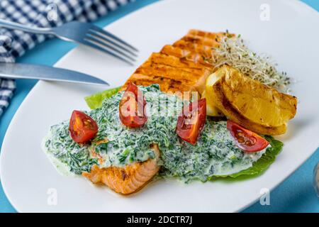 Gegrilltes Lachssteak. Ein Stück roter Fisch auf einem weißen Teller und ein blauer Hintergrund auf dem Tisch. Fischfutter mit Sauce, Tomaten, Zitrone. Speisekarte im Restaurant Stockfoto