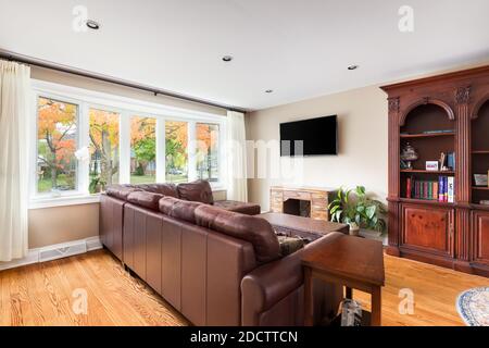 Ein gemütliches Wohnzimmer mit einer Ledercouch vor einem Fernseher und Blick auf einige schöne, bunte Herbstblätter draußen. Stockfoto