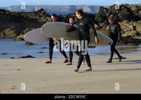 Surfer tragen ihre Surfbretter und laufen am Great Western Beach in Newquay in Cornwall. Stockfoto