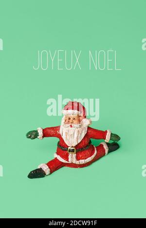 Eine Figur des weihnachtsmanns springen oder in einer Spalte Und der Text fröhliche weihnachten in französisch auf einem geschrieben Grüner Hintergrund Stockfoto