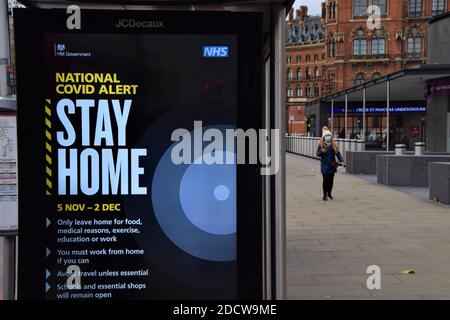 Eine Frau mit einer schützenden Gesichtsmaske geht während der zweiten nationalen Sperre in England an einem Stay Home-Schild an einer Bushaltestelle in King's Cross vorbei. London, Großbritannien 21. November 2020. Stockfoto