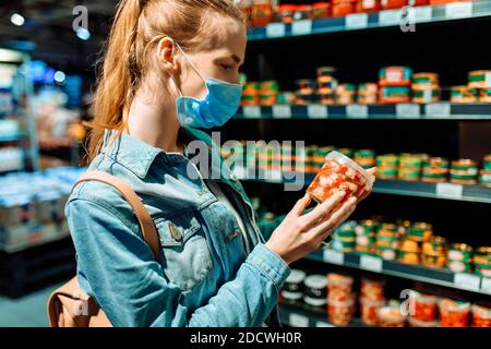 Junge Frau in einer medizinischen Schutzmaske auf ihrem Gesicht kauft Lebensmittel in einem Supermarkt. Eine junge Dame wählt Meeresfrüchte in einem Lebensmittelgeschäft. Verkauf, Kauf, Verkauf Stockfoto