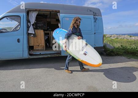 Junge Erwachsene männliche Surfer in Neoprenanzug setzen Surfbrett aus dem Van Fahrzeug am Fistral Beach in Newquay, Cornwall, Großbritannien Stockfoto