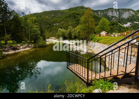 Hölzerner Aussichtspunkt über einem kleinen Fluss mit weißen runden Steinen Am Ufer des Triglav Nationalparks in Slowenien Am bewölkten Herbsttag Stockfoto