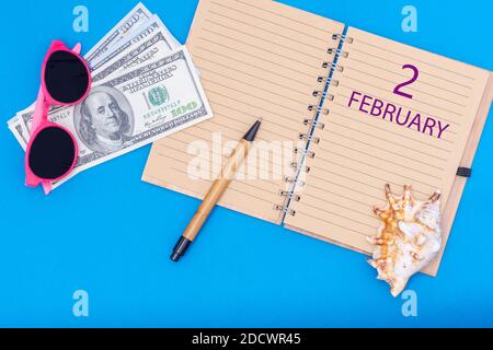 Februar. Tag Februar. Reiseplan flaches Design mit Notizblock Schreibdatum, Stift, Brille, Gelddollar und Muschel auf blauem Hintergrund. Winte Stockfoto