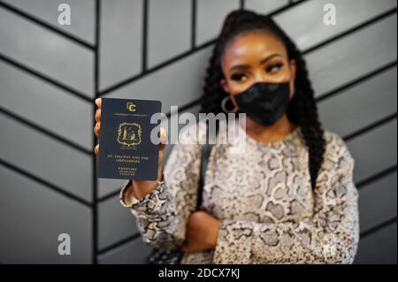 afroamerikanische Frau mit schwarzer Gesichtsmaske zeigt St. Vincent und die Grenadinen Pass in der Hand. Coronavirus in Amerika Land, Grenzschließung Stockfoto