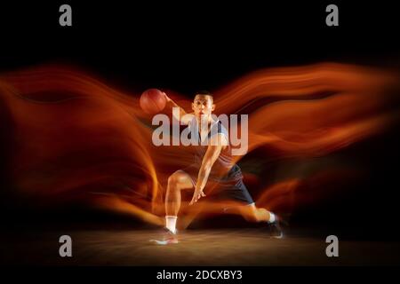 Führung. Junge ostasiatische Basketballspieler in Aktion und Bewegung Springen in gemischtem Licht über dunklen Studio-Hintergrund. Konzept von Sport, Bewegung, Energie und dynamischen, gesunden Lebensstil. Stockfoto
