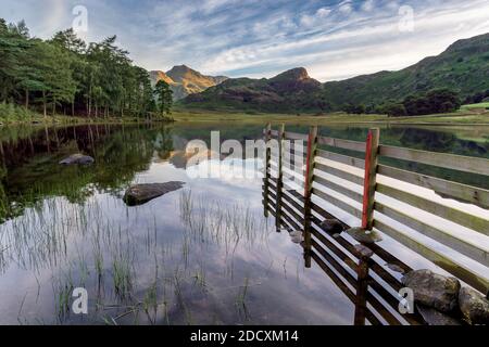 Holzzaun führt zu einer schönen Aussicht auf Blea Tarn und die Langdale Pikes mit perfekten Reflexionen. Lake District, Großbritannien. Stockfoto