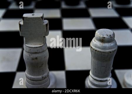 König und Königin auf einem abgenutzten hölzernen Schachbrett, allein stehend gegen Opposition. Stockfoto