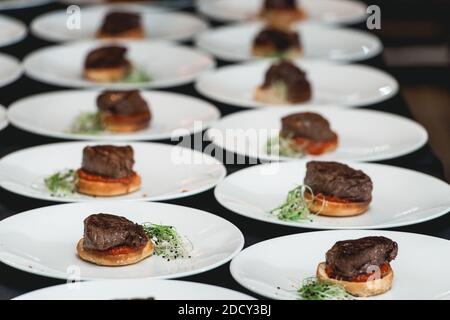 Koch in schwarzen Handschuhen serviert Burger auf dem Tisch in einem Restaurant. Schwarze Tischdecke Stockfoto