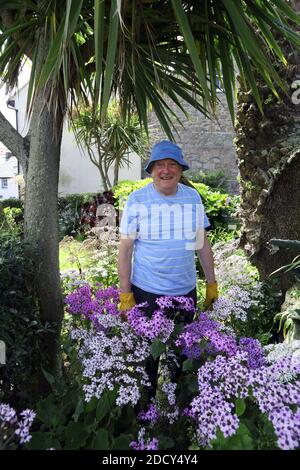 GROSSBRITANNIEN / Isles of Scilly/ St Mary's/ Reife männliche Gärtnerin mit gelben Handschuhen steht in seinem Garten. Stockfoto