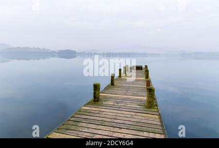 Langer hölzerner Steg an einem nebligen Frühlingsmorgen in Windermere im Lake District, Großbritannien. Stockfoto