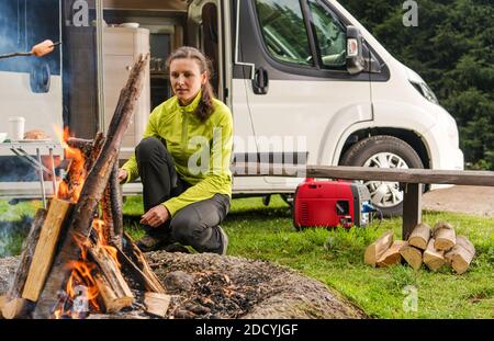 Alleinstehende kaukasische Frau in ihren 30er Jahren mit Wohnmobil Wohnmobil Wohnmobil Wohnmobil, Camping allein und die Zubereitung von Lebensmitteln am Lagerfeuer. Campingplatz und Urlaub Thema. Stockfoto