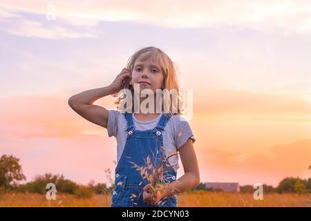 Blonde Mädchen auf einer Herbstwiese bei Sonnenuntergang mit Ähren aus Weizen in der Hand, richtet ihr Haar. Stockfoto