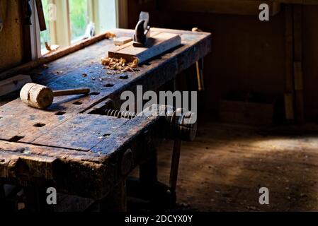 Tischlerwerkstatt mit Werkzeugen und Holzschnitzereien auf dem Tisch verstreut und natürliches Sonnenlicht strömt herein. Stockfoto