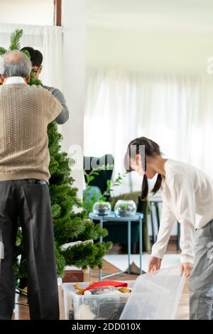 Mehrgenerationenübergreifende asiatische Familie, die einen Weihnachtsbaum schmückt. Mama Papa Tochter Mädchen und Großvater schmücken den Weihnachtsbaum Vorbereitung für die Saison begrüßen Stockfoto