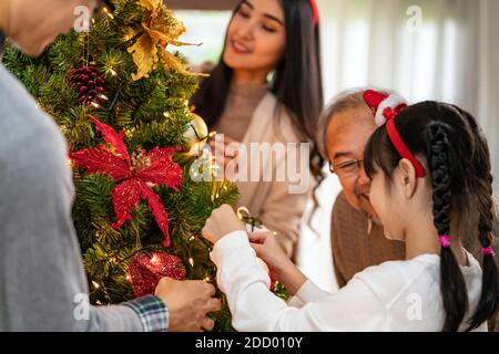 Mehrgenerationenübergreifende asiatische Familie, die einen Weihnachtsbaum schmückt. Mama Papa Tochter Mädchen und Großvater schmücken den Weihnachtsbaum Vorbereitung für die Saison begrüßen Stockfoto