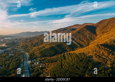 Luftaufnahme der herbstlichen Berglandschaft und Asphaltstraße am Fuße der Bergkette, Reise- und Freiheitskonzept. Stockfoto