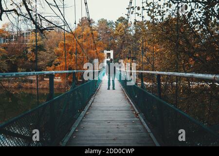 Alte Hängebrücke über den Fluss und der Mensch geht am grauen Herbsttag. Melancholie, Depression oder Einsamkeit. Stockfoto