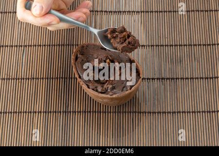 Die rechte Hand des Erwachsenen nimmt die Füllung des Ostereiers mit einem Metalllöffel auf. Füllung aus dunkler Schokolade und Nüssen. Traditionelle brasilianische Süßigkeit. Stockfoto