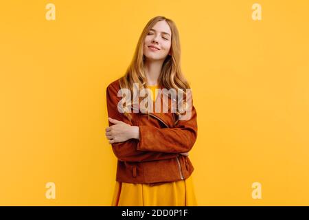 Attraktive, nachdenkliche, verträumte Mädchen in einem leuchtend gelben Kleid und Herbstjacke Posen auf einem gelben Hintergrund. Das Konzept des Herbstes Stockfoto