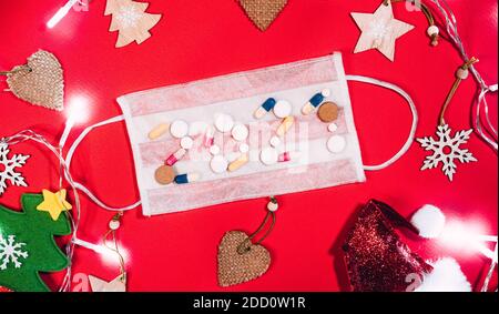 Die Inschrift 2021 von Tabletten auf einer weißen Schutzmaske auf einem roten Hintergrund und Weihnachtsschmuck um. Niedlicher Weihnachtsmütze, kleiner Christm Stockfoto