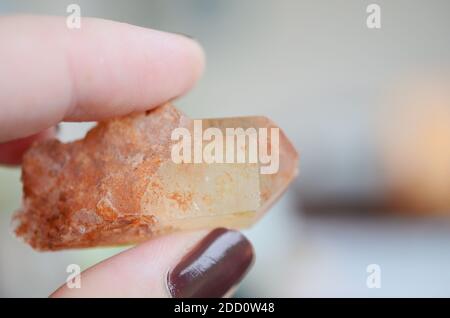 Die Hand der Frau hält die Quarzpunkte der Mandarine. Orangefarbene Quarzpunkte bei Tageslicht. Orange heilende Kristallpunkte, unkonventionelle Einrichtung, Hexenkrys Stockfoto