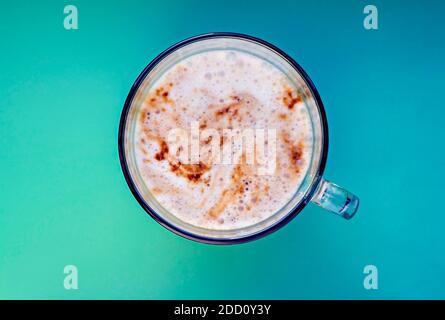 Tasse Cappuccino mit Schaum Nahaufnahme auf blaugrünem Hintergrund. Kaffee in einer Glaskanne, Draufsicht, Kopierraum, Heißgetränk Stockfoto