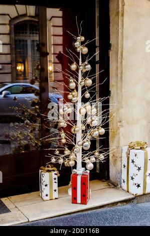 Kreative Weihnachtsbaum draußen. Alternativer Weihnachtsbaum aus Metall mit festlichen Bällen und Geschenkkartons nahe dem Vordereingang zur Café-Fassade. Weihnachten Stockfoto